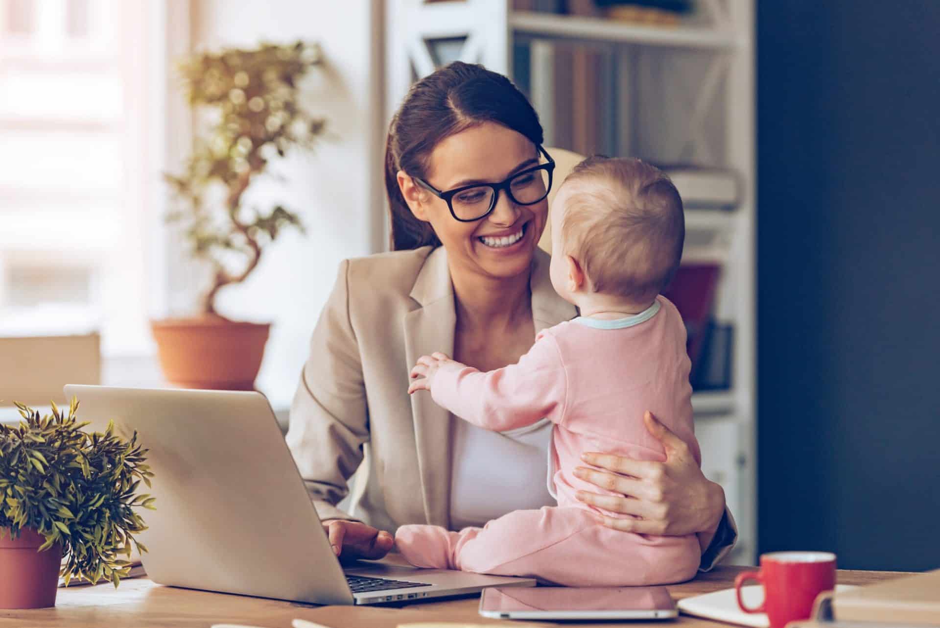 Mother working on laptop while playing with baby on desk
